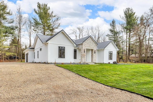 modern farmhouse style home with metal roof, driveway, a front lawn, and stone siding