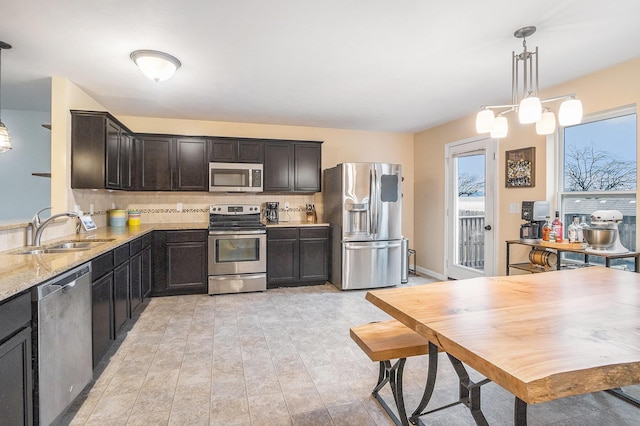 kitchen featuring stainless steel appliances, a sink, hanging light fixtures, light stone countertops, and tasteful backsplash