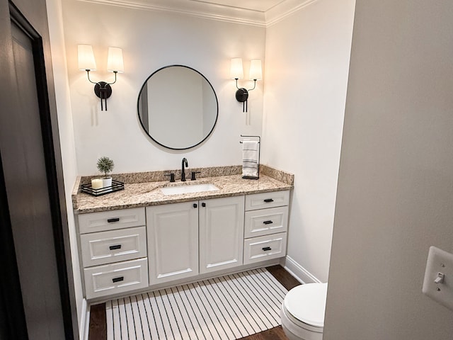 half bathroom with vanity, wood finished floors, baseboards, crown molding, and toilet