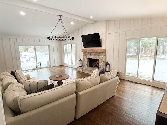 living area featuring a stone fireplace, lofted ceiling with beams, dark wood-type flooring, and a chandelier