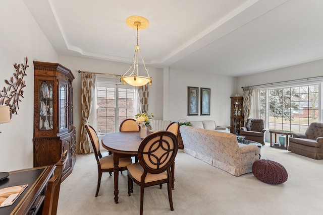 dining space featuring a raised ceiling, light colored carpet, and a healthy amount of sunlight