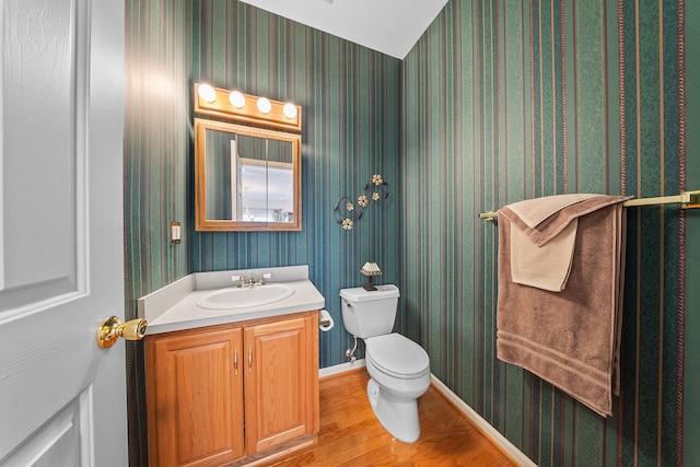 bathroom featuring vanity, wood finished floors, toilet, and wallpapered walls