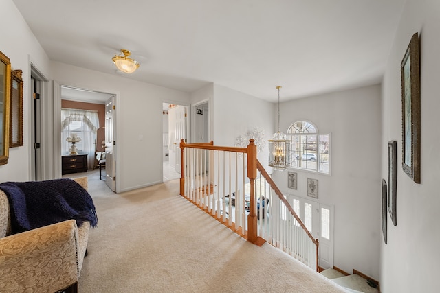 hall with an upstairs landing, baseboards, an inviting chandelier, and light colored carpet