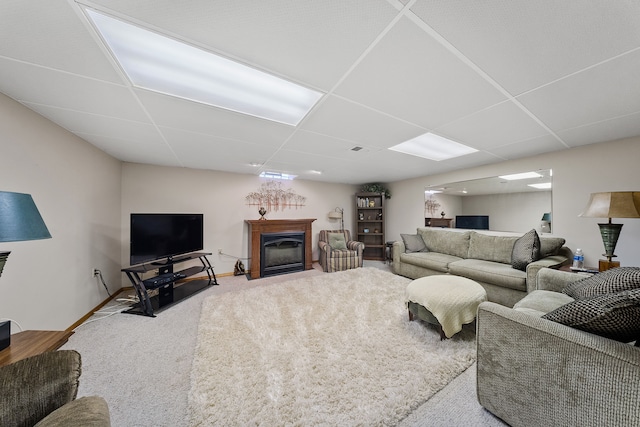 living room with baseboards, a drop ceiling, carpet flooring, and a glass covered fireplace