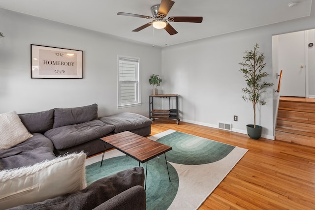 living area with a ceiling fan, wood finished floors, visible vents, baseboards, and stairs