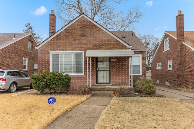 bungalow-style house with roof with shingles, a chimney, a front lawn, and brick siding