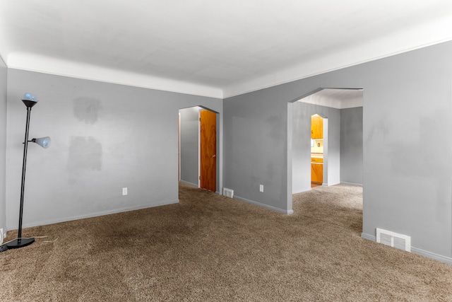 carpeted spare room featuring arched walkways, visible vents, and baseboards