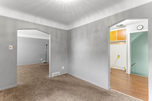 carpeted spare room with arched walkways, visible vents, and baseboards