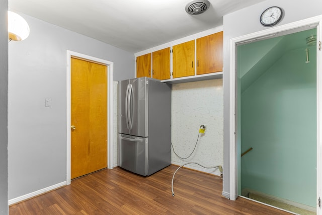 kitchen with dark wood-style flooring, visible vents, baseboards, freestanding refrigerator, and brown cabinets