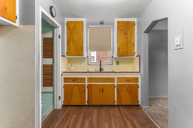 kitchen featuring a sink, brown cabinetry, backsplash, and dark wood-style flooring