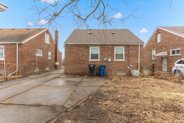 rear view of house with cooling unit, brick siding, fence, and roof with shingles