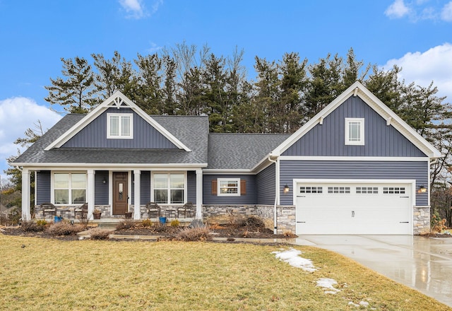 craftsman-style home with driveway, a shingled roof, stone siding, covered porch, and a front yard