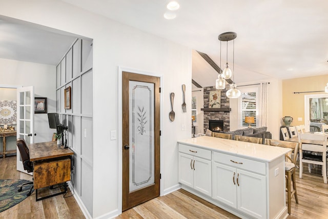 kitchen with a stone fireplace, a peninsula, white cabinetry, light wood finished floors, and a kitchen bar