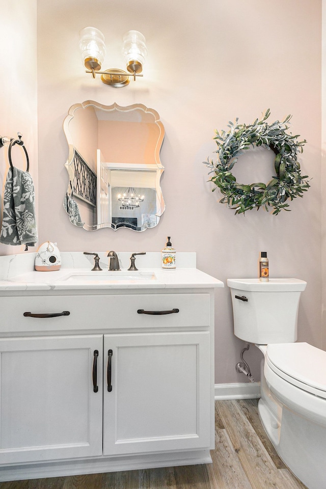 half bathroom with baseboards, vanity, toilet, and wood finished floors