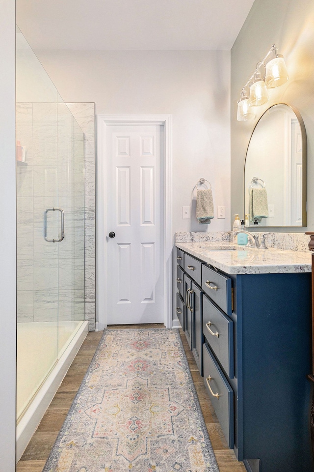 full bath with baseboards, vanity, a shower stall, and wood finished floors