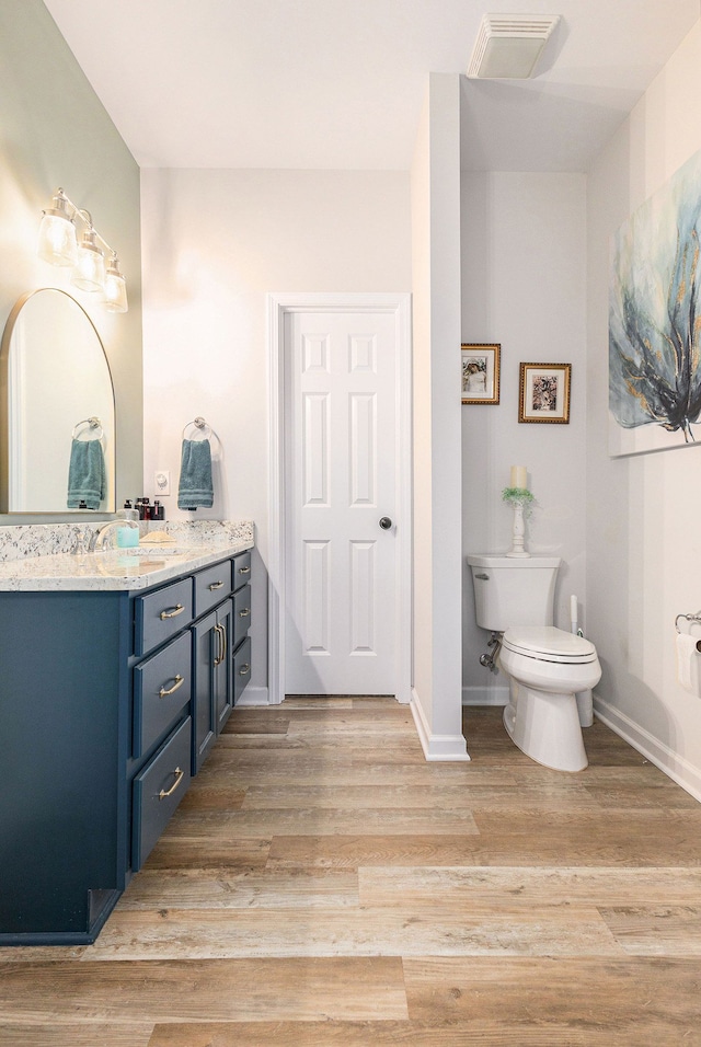 bathroom with baseboards, visible vents, toilet, wood finished floors, and vanity