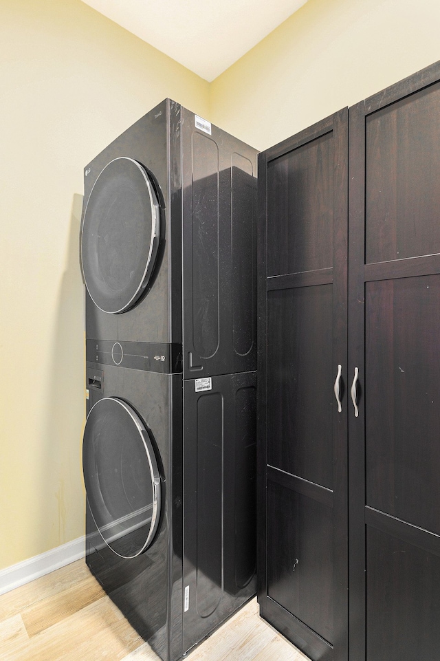 laundry room featuring cabinet space, baseboards, light wood finished floors, and stacked washer / dryer