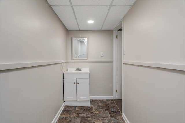 bathroom featuring a drop ceiling, baseboards, vanity, and stone finish floor