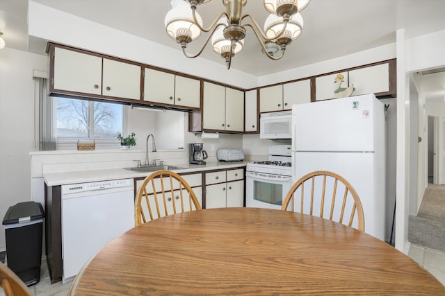 kitchen featuring white appliances, a sink, light countertops, white cabinets, and a notable chandelier