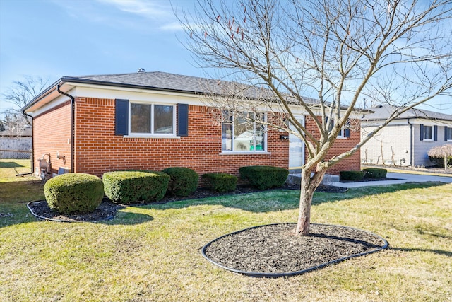 ranch-style house featuring a front yard, fence, brick siding, and roof with shingles