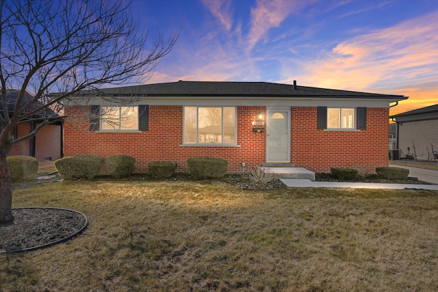 view of front of home with a yard, brick siding, and a shingled roof