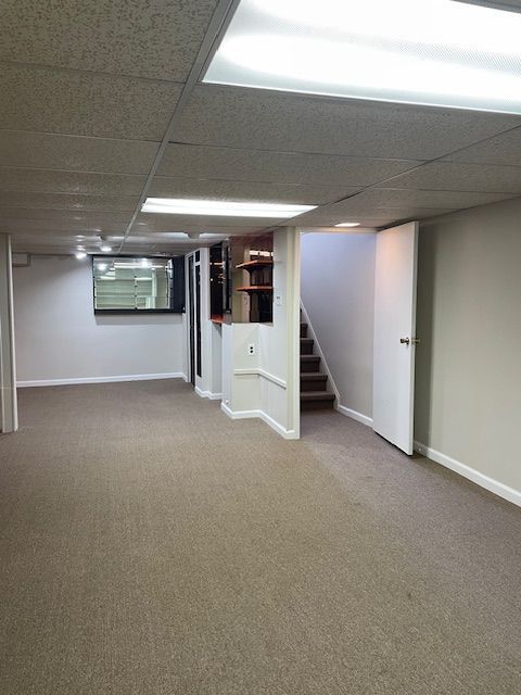 finished basement with stairs, carpet flooring, a paneled ceiling, and baseboards