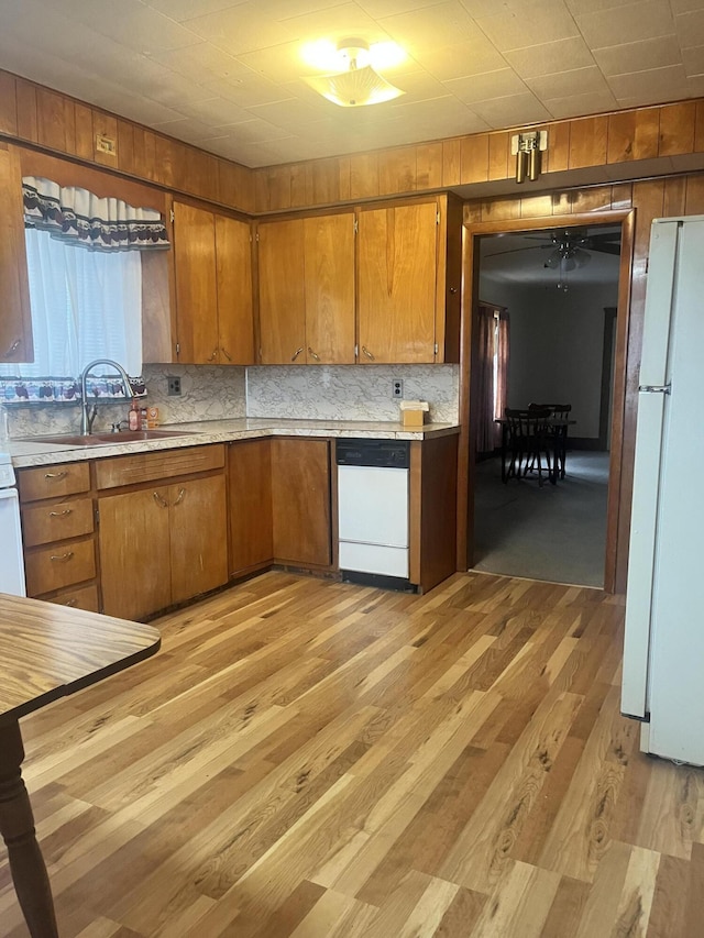 kitchen featuring brown cabinets, light countertops, light wood-style flooring, a sink, and white appliances