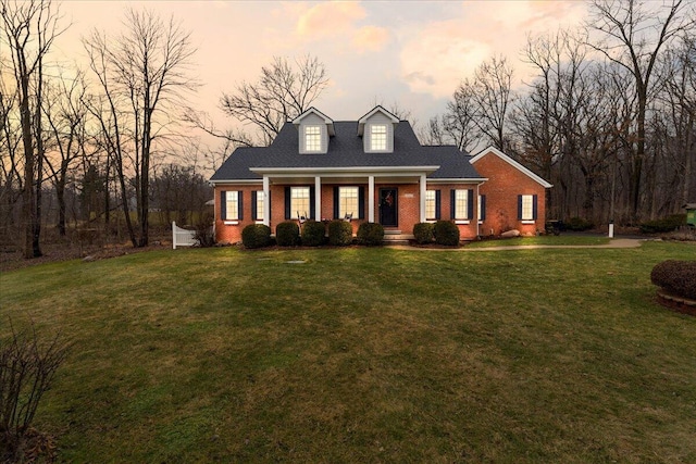 new england style home with covered porch, brick siding, and a front lawn