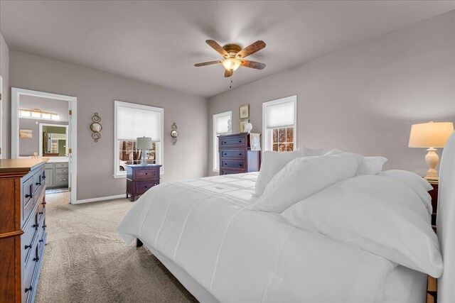 bedroom featuring light carpet, ensuite bath, a ceiling fan, and baseboards