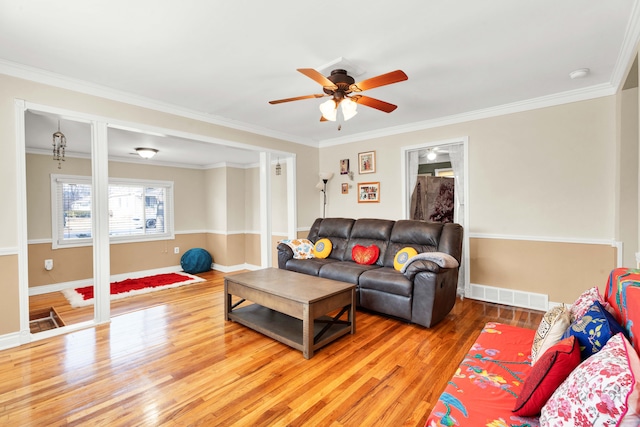 living room featuring baseboards, light wood-style flooring, visible vents, and crown molding