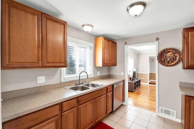 kitchen featuring brown cabinets, light tile patterned floors, visible vents, stainless steel dishwasher, and a sink