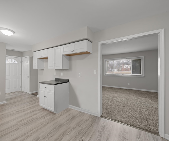 kitchen with light wood-style flooring, dark countertops, white cabinetry, and baseboards