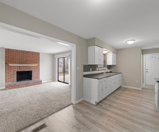 kitchen featuring light carpet, a sink, visible vents, a brick fireplace, and tasteful backsplash