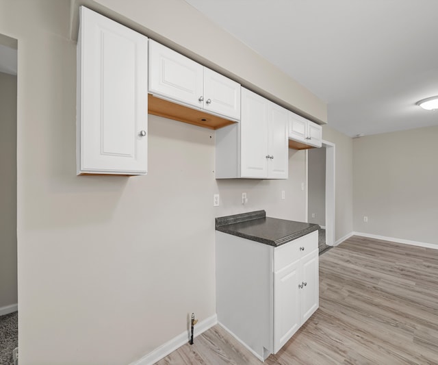 kitchen with light wood-style flooring, dark countertops, white cabinetry, and baseboards