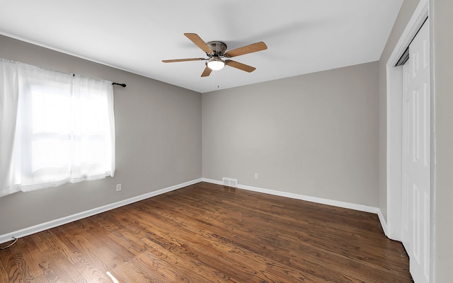 empty room with ceiling fan, visible vents, baseboards, and dark wood-style floors