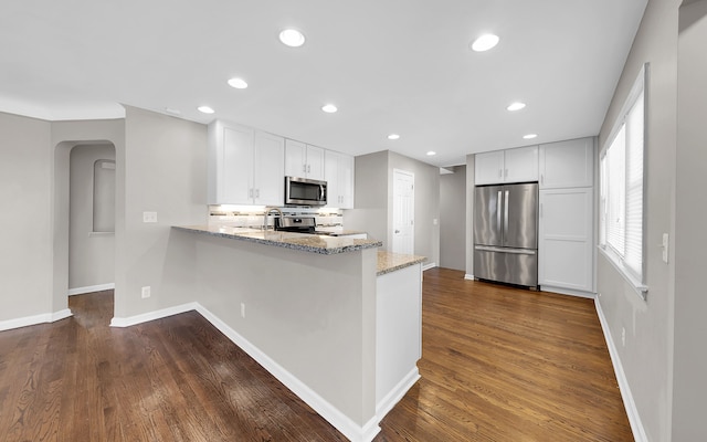 kitchen with dark wood-style floors, light stone countertops, a peninsula, arched walkways, and stainless steel appliances