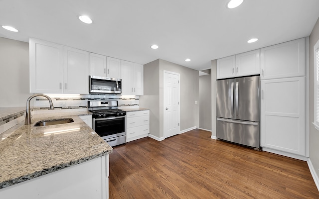 kitchen featuring a sink, light stone counters, decorative backsplash, appliances with stainless steel finishes, and dark wood-style flooring