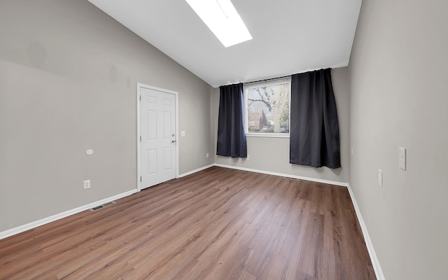 empty room with visible vents, vaulted ceiling with skylight, baseboards, and wood finished floors