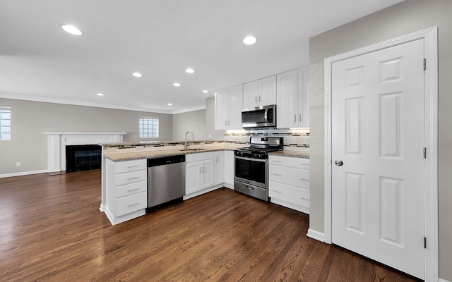 kitchen with dark wood finished floors, appliances with stainless steel finishes, a peninsula, white cabinets, and a sink