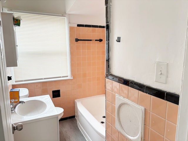 bathroom with vanity, a bath, wood finished floors, tile walls, and toilet