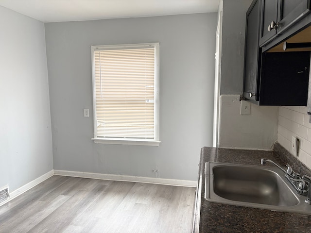 kitchen with light wood finished floors, dark countertops, baseboards, and a sink