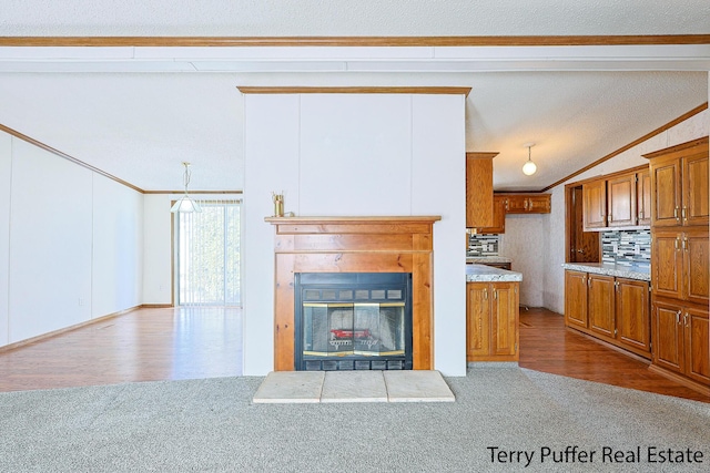 unfurnished living room featuring dark carpet, ornamental molding, vaulted ceiling, and a glass covered fireplace