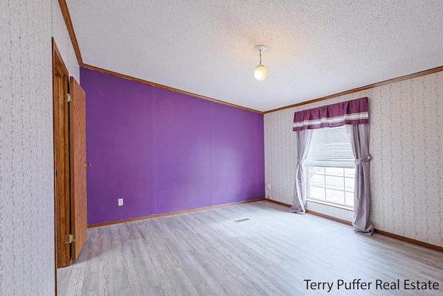 unfurnished room with a textured ceiling, wood finished floors, baseboards, ornamental molding, and wallpapered walls