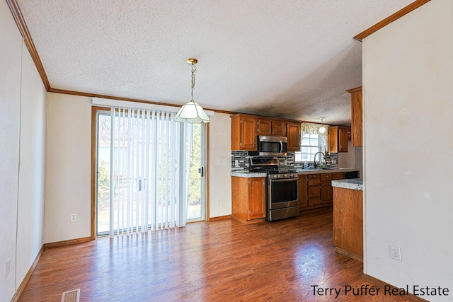 kitchen featuring brown cabinets, dark wood-style flooring, stainless steel appliances, crown molding, and backsplash