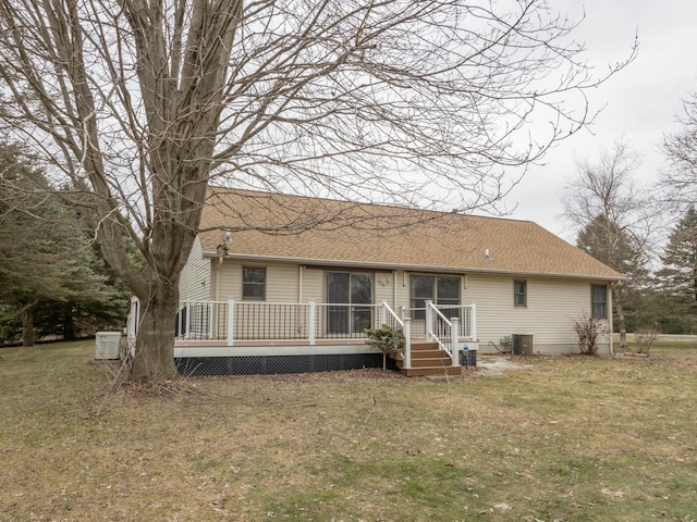 rear view of property featuring roof with shingles, a yard, a deck, and central AC unit