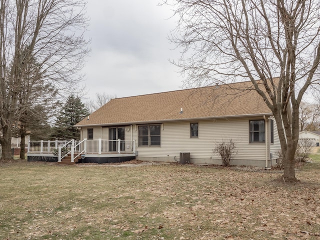 back of property with a wooden deck, roof with shingles, central AC, and a yard