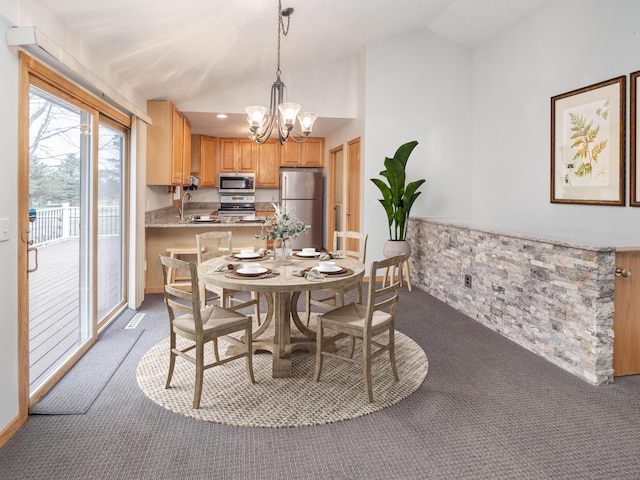 carpeted dining area with a chandelier, wainscoting, vaulted ceiling, and a sink