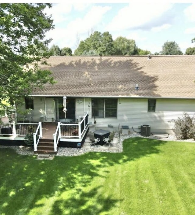 back of property with central AC unit, a wooden deck, roof with shingles, and a yard