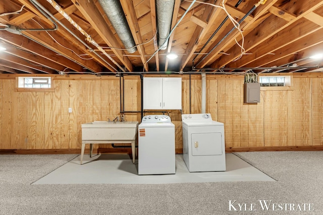 clothes washing area featuring wooden walls, laundry area, a sink, electric panel, and washer and clothes dryer