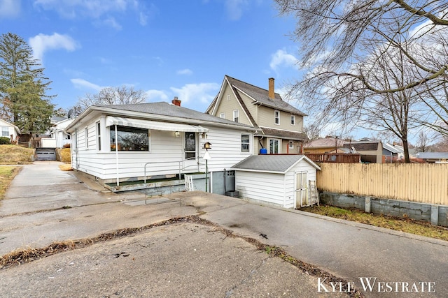 view of front of house featuring driveway, a storage shed, a chimney, fence, and an outdoor structure